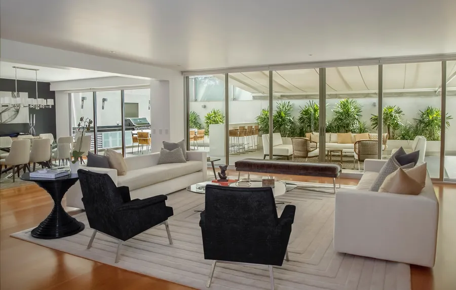 A large, tidy living room with white sofas, two dark armchairs and glass doors onto a planted patio.