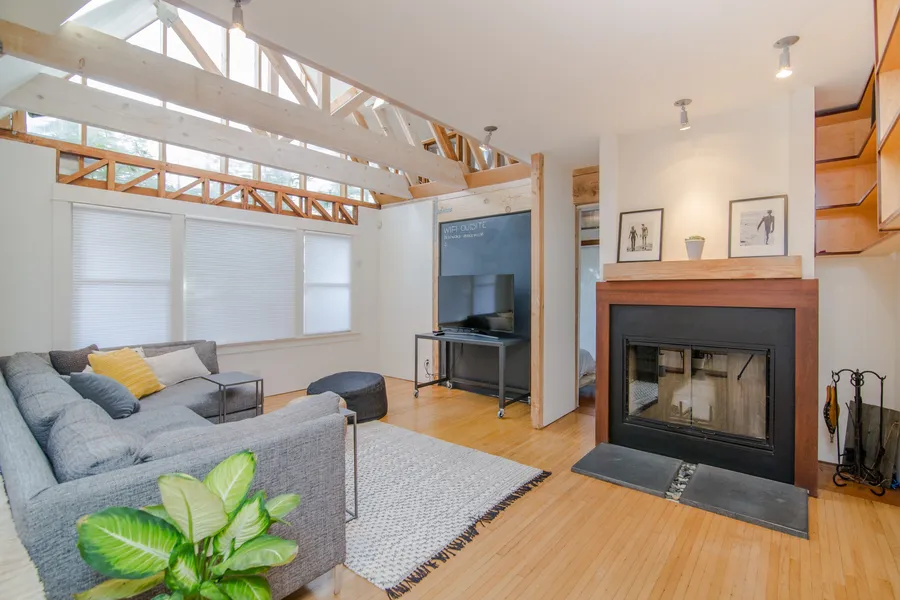 A sunlit loft living room with a grey sectional sofa, a woven rug and a fireplace.